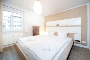 Camera d'albergo con un ampio letto, un comodino, una finestra con tende e una mensola a parete.