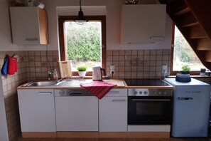 A kitchen with a sink, stove, and refrigerator. There is a window with a view of greenery outside. - to the view of the sun (Kröpelin, OT Wichmannsdorf)