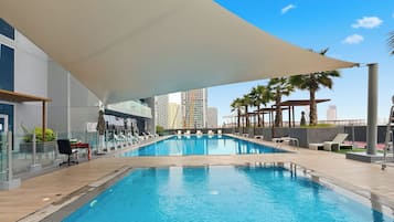 Une piscine dotée d’un parasol, de chaises longues et offrant une vue sur les grands immeubles qui se dressent à l’arrière-plan.