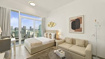 A hotel room with a bed, a sofa, a coffee table, a desk, and a chair. There is a large window with a city view.