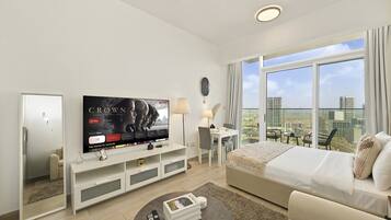 A modern hotel room with a large TV, a bed, a seating area, and a balcony with a city view.