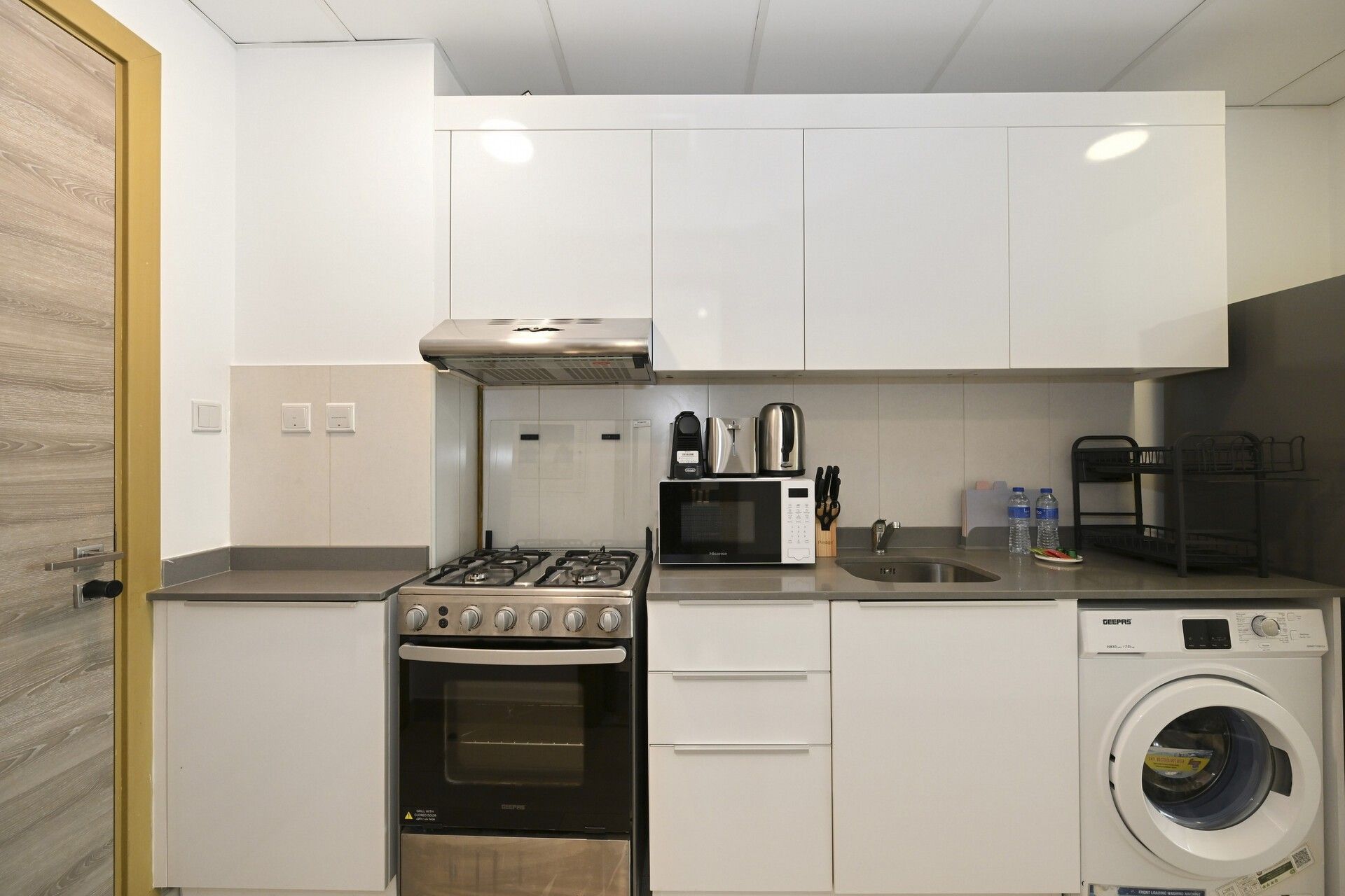A compact kitchen with a gas stove, microwave, oven, and a front-loading washing machine.
