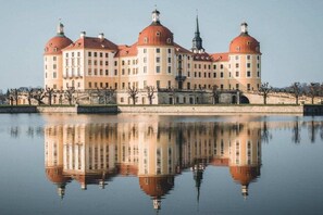 Ein großes, historisches Gebäude mit mehreren Kuppeln und Spiegelung im Wasser.