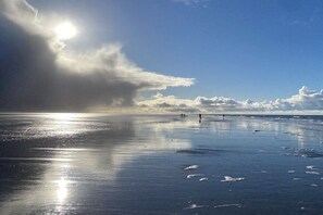 Ein Strand mit blauem Himmel, ruhigem Wasser und einigen Spaziergängern.