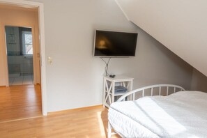 Ein Schlafzimmer mit einem Bett, einem an der Wand befestigten Fernseher und einem weißen Nachttisch.