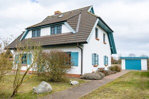 A two-story house with a sloped roof, a visible chimney, and a front garden with a pathway leading to the entrance. - House by the paddock (Born\/ DarßMit)