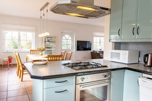 Eine moderne Küche mit Gaskochfeld, Backofen und Mikrowelle. Ein Essbereich mit Tisch und Stühlen vorhanden.