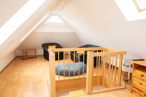 Ein Schlafzimmer im Loft-Stil mit schrägem Dach, einem Holz-Babybett, einem schwarzen Sofa und einem kleinen Tisch.