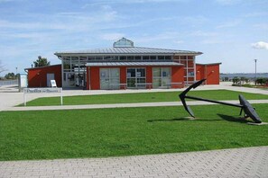Ein rotes Gebäude mit Glastür, einer Grünfläche davor und einer Metallskulptur.