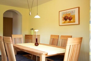 A dining area with a wooden table and chairs, a vase with flowers, and a painting on the wall. - Thaneller Guesthouse Müller (Bichlbach)