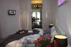 Ein Hotelzimmer mit einem Bett, einem Nachttisch mit Lampe, einem Rosenstrauß und einem an der Wand befestigten Fernseher.
