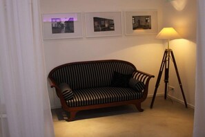A room with a striped sofa, a floor lamp, and three framed pictures on the wall. - Holiday apartment with 1 bedroom (Werder\/Havel)