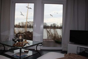 A room with a glass table, a television, and a view of a lake with birds. - Holiday apartment with 1 bedroom (Werder\/Havel)