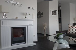 A modern living room with a fireplace, a glass coffee table, and a sofa with patterned cushions. - 110m² harbor suite with 2 bathrooms (Wismar)
