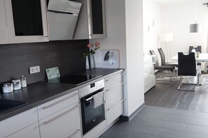 A modern kitchen with a built-in oven, a stainless steel range hood, and a dining area with a table and chairs. - 110m² harbor suite with 2 bathrooms (Wismar)