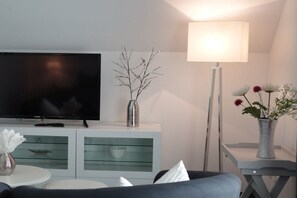 A modern living room with a flat-screen TV, a white cabinet with glass doors, a floor lamp, and a vase with flowers. - 110m² harbor suite with 2 bathrooms (Wismar)