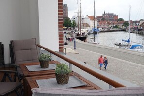 A balcony with wooden furniture and potted plants, overlooking a marina with boats and a town in the background. - 110m² harbor suite with 2 bathrooms (Wismar)