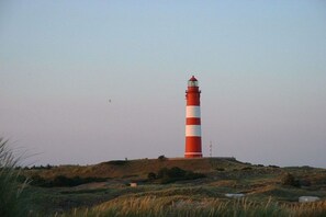 A tall lighthouse with a red and white striped pattern, situated on a grassy hill with a clear sky. - Holiday apartment with 2 bedrooms (Nebel \/ Amrum)