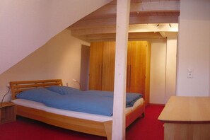A single bed in a room with a sloped ceiling, wooden wardrobe, and a small table. - Holiday apartment with 2 bedrooms (Nebel \/ Amrum)
