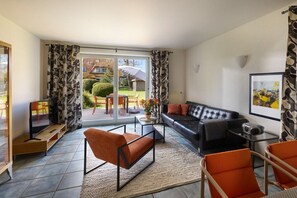 Ein modernes Wohnzimmer mit einer Couch, Sesseln, einem Fernseher und einer Schiebetür zu einem Garten.