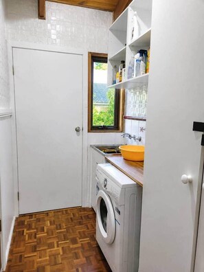 Ein kleiner Hauswirtschaftsraum mit Waschmaschine, Spüle und Fenster.