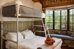Een stapelbed met een ladder, een raam met een stenen muur en een bankje.