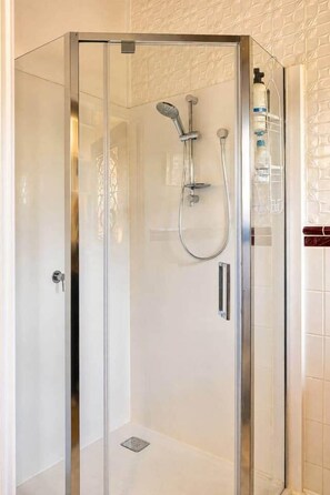 Een douchecabine met glazen wanden, een handdouche en een kraan op de muur.