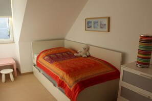 Ein Schlafzimmer mit einem Bett, einem kleinen Schreibtisch, einem Stuhl, einer Kommode und einem Fenster.