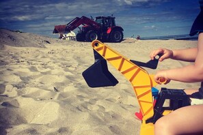 A sandy beach with a toy excavator and a red vehicle in the background. - Beach House Sea Treasure (Graal-Müritz)