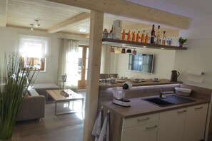 Une cuisine moderne équipée d’un four encastré, d’un évier et d’un plan de travail agrémenté de divers ustensiles de cuisine. On y trouve également un coin repas avec un canapé et une table basse.
