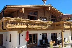 A wooden chalet with a balcony, outdoor seating, and a red umbrella. - Hochalmbahnen Chalet (Rauris)