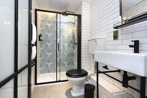 Uma casa de banho moderna com cabine de duche em vidro, sanita branca e lavatório branco com torneira preta.