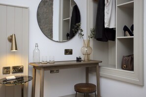 A room with a round mirror, a wooden table, a stool, a shelf with shoes, and a window with a view. - Georgian Apt w/ Courtyard Near Edinburgh Castle (Edinburgh)