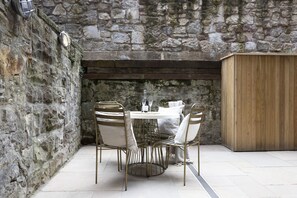 A stone-walled outdoor dining area with a round table and four chairs, a wooden cabinet, and a stone wall. - Georgian Apt w/ Courtyard Near Edinburgh Castle (Edinburgh)