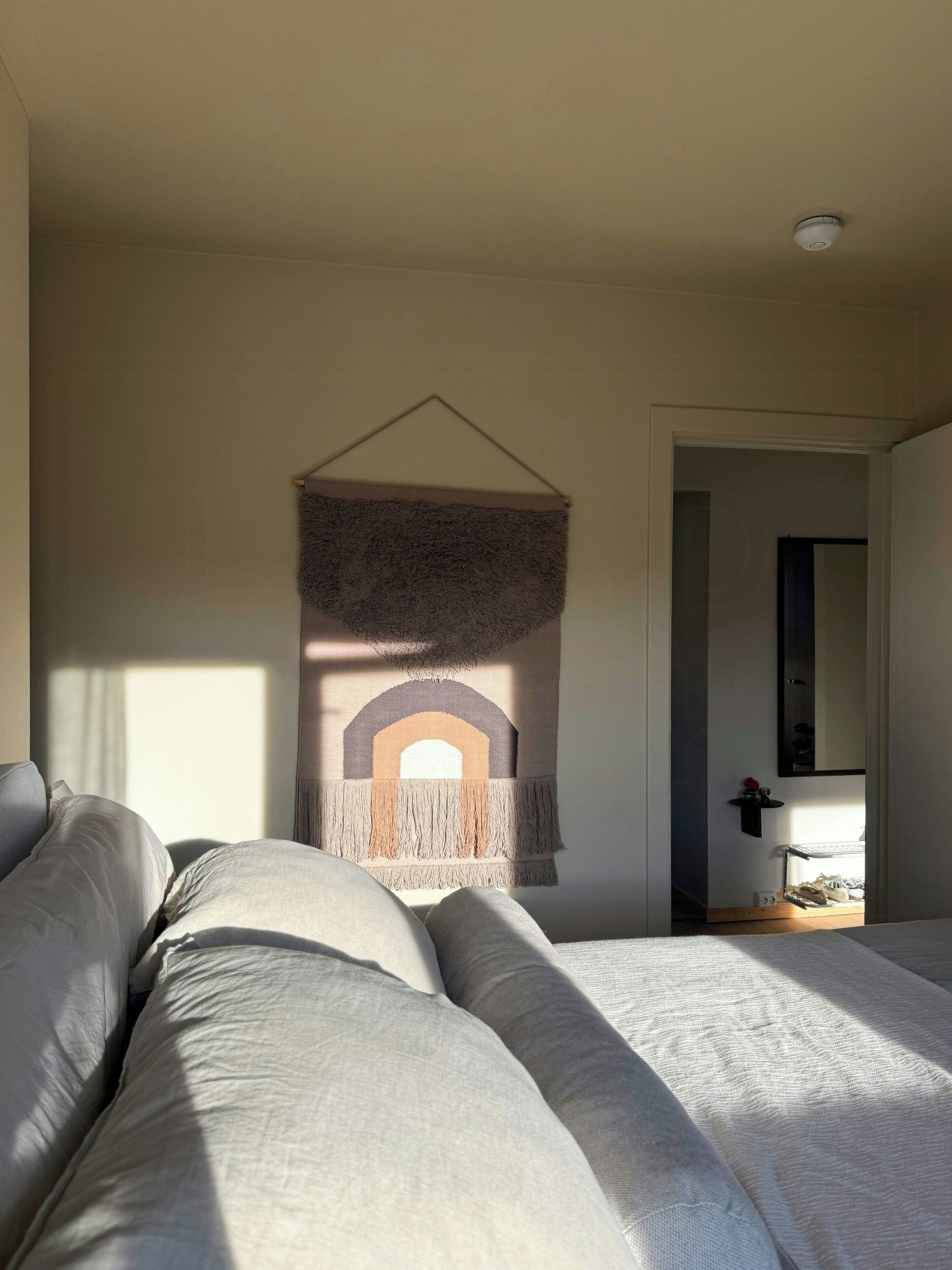 A bedroom with a bed, a wall-mounted tapestry, and a door leading to another room.