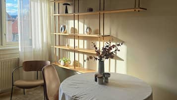 A room with a round table, two chairs, a bookshelf, and a window with curtains.