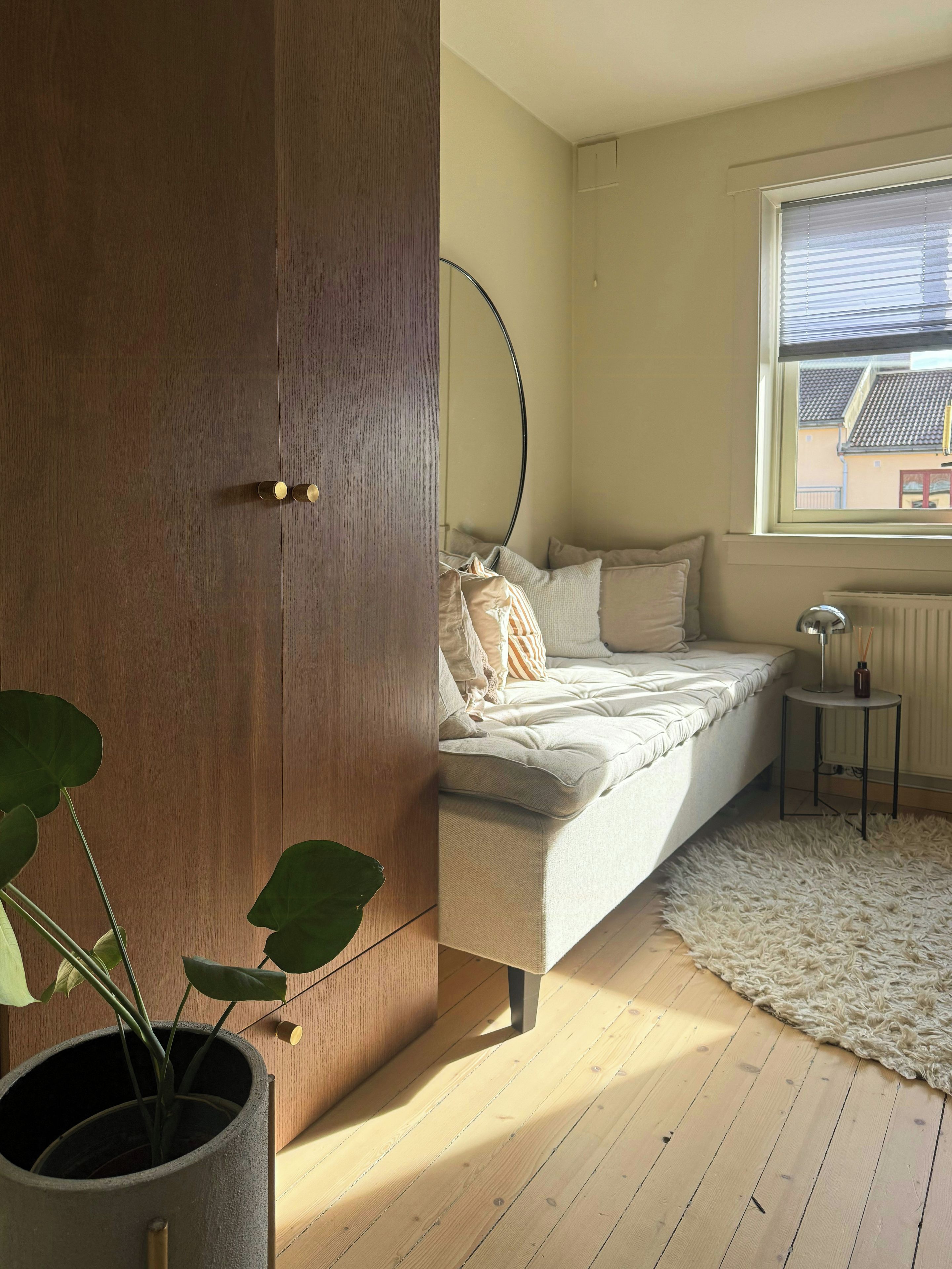 A bedroom with a bed, a potted plant, a radiator, and a window.