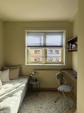 Un dormitorio con cama, escritorio, silla, radiador y ventana con persianas.