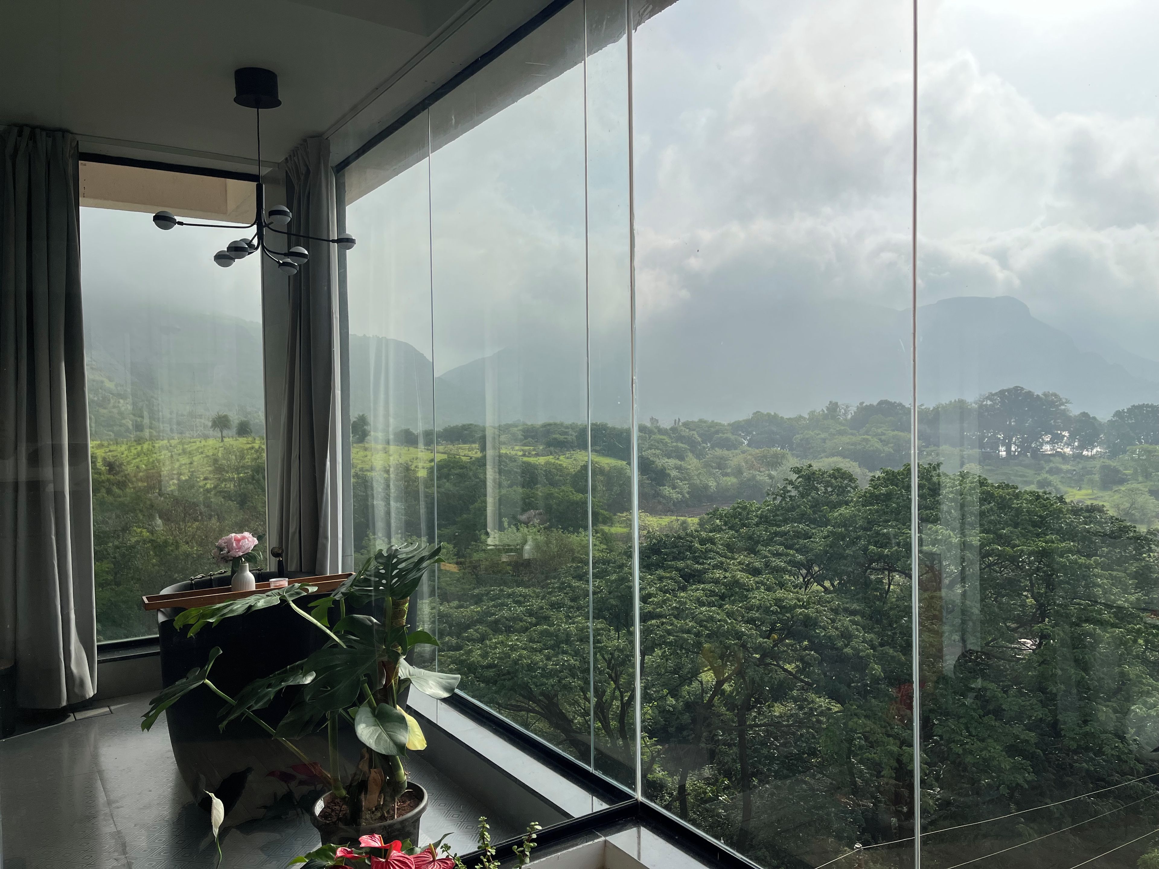 A room with a large window overlooking a lush landscape, a potted plant, and a vase with a flower.