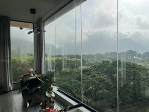 Une pièce dotée d’une grande fenêtre donnant sur un paysage verdoyant, avec une plante en pot et un vase contenant une fleur.