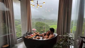 Una pareja en una bañera con vistas a un paisaje verde a través de un ventanal grande.