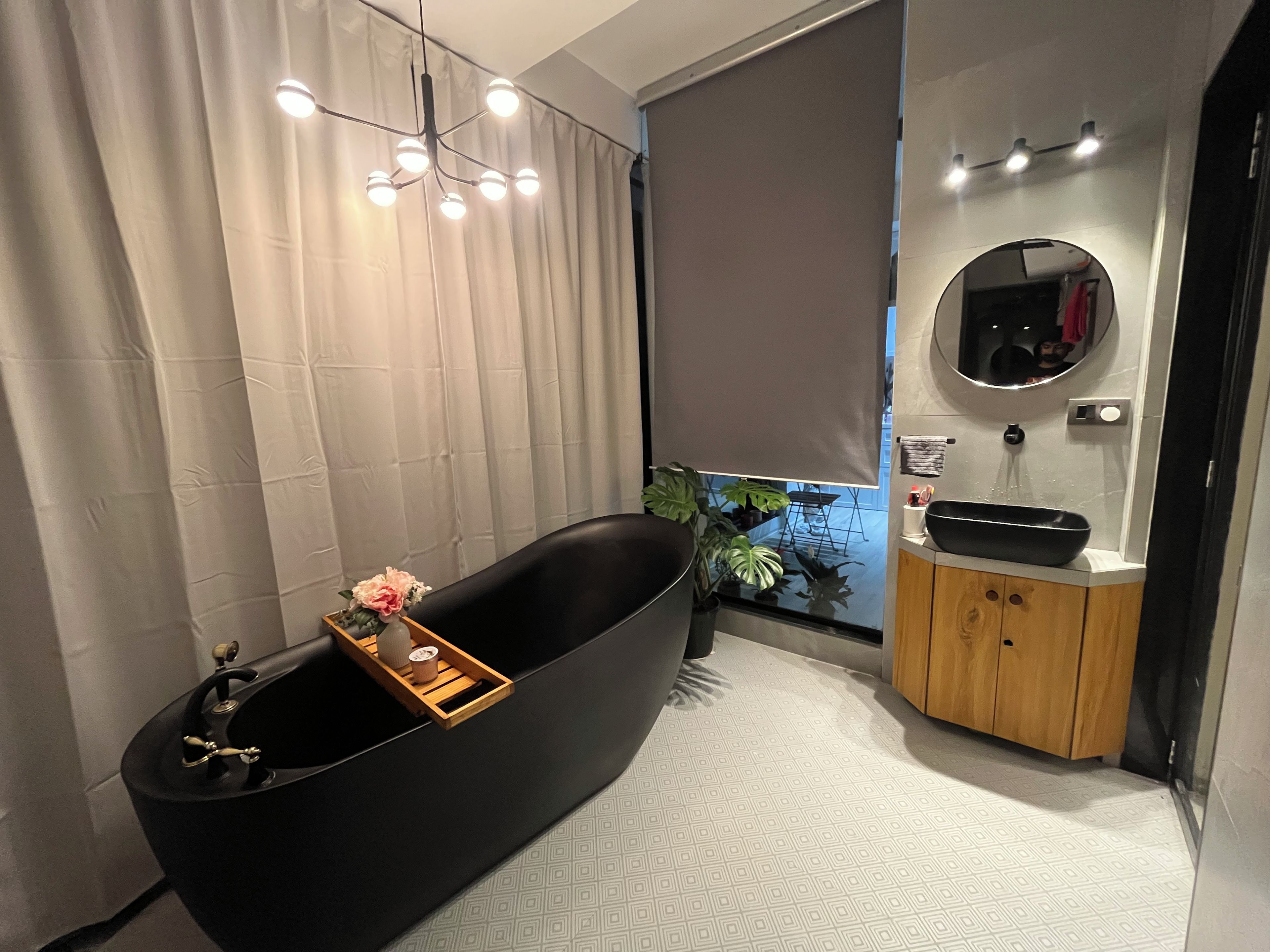 Une salle de bain moderne avec une baignoire noire, un meuble-lavabo en bois, un miroir et un luminaire au plafond.