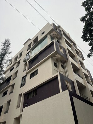 A multi-story building with balconies, large windows, and a modern architectural style. - Cozy 1-bedroom kitchen apartment in peaceful Igatpuri with bathtub and AC (Igatpuri)