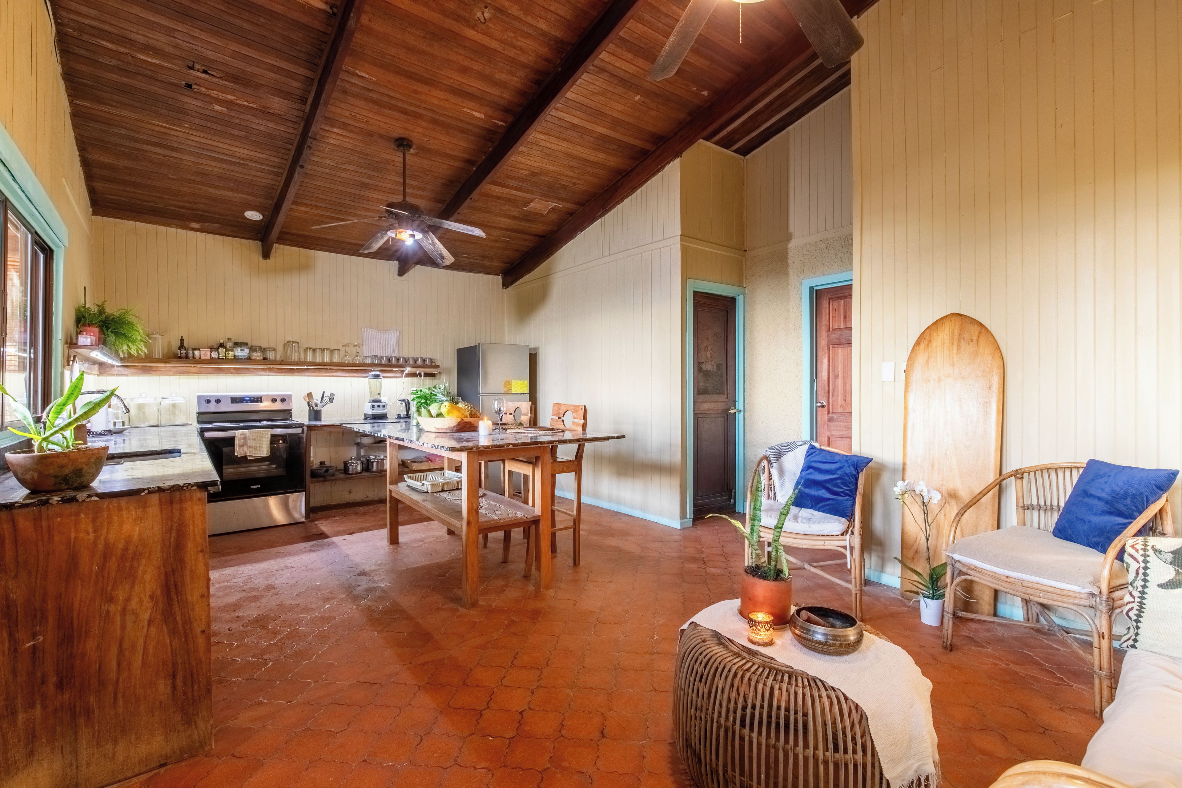 Uma cozinha espaçosa com armários de madeira, uma sala de jantar com mesa e cadeiras, e uma sala de estar com móveis de vime.