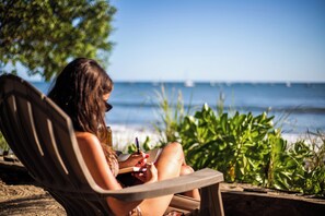 Eine Person sitzt am Strand auf einem Stuhl und liest ein Buch.