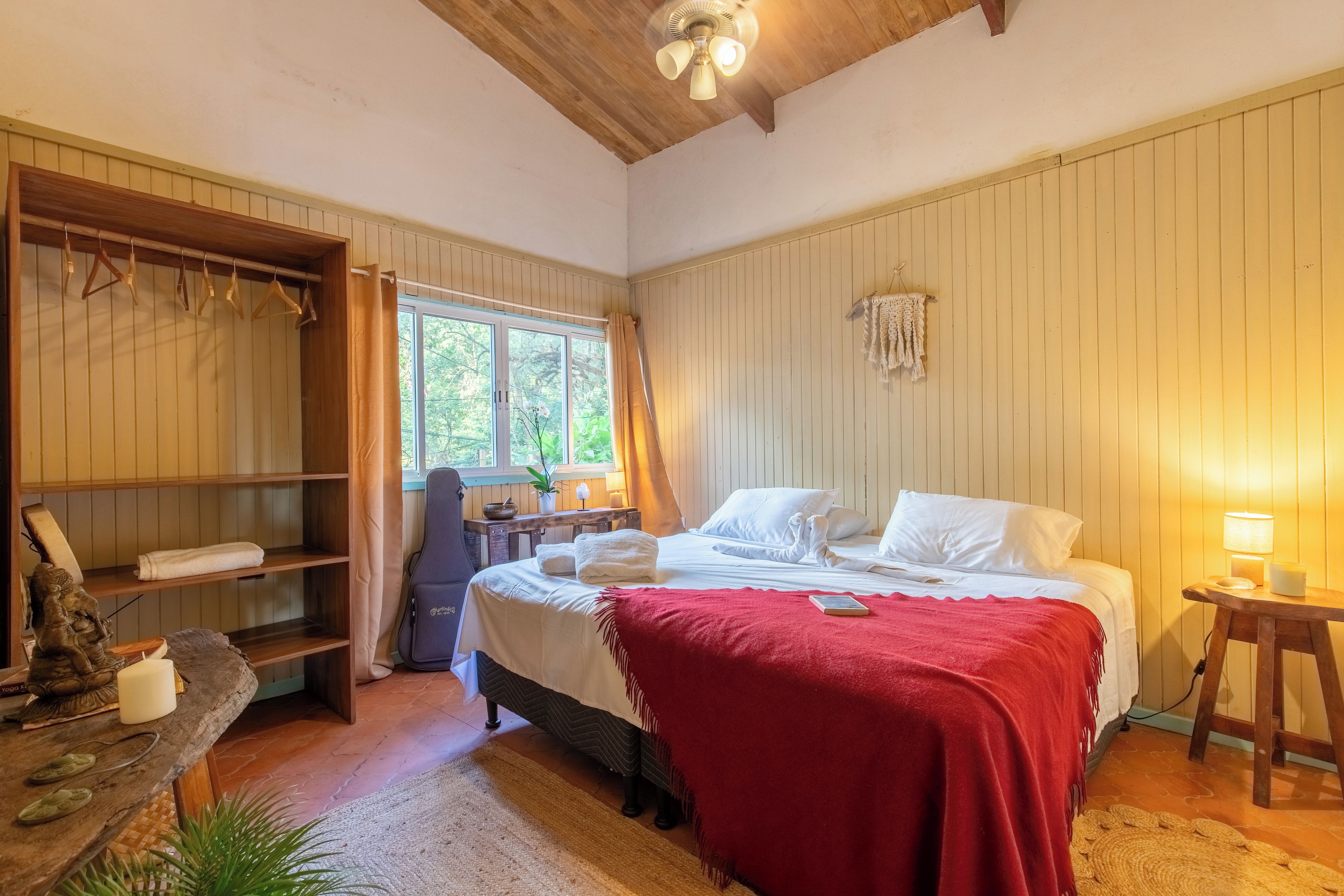 Quarto com cama, guarda-roupa de madeira, escrivaninha e janela.