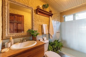 Ein Badezimmer mit einem Holz-Waschtisch, einem großen Spiegel, einer Toilette, einer Dusche und einem Regal mit Pflanzen.