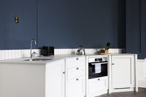 A modern kitchen with a white countertop, a double sink, a built-in oven, and a microwave. - Edinburgh Apartment: Steps to Castle, Modern (Edinburgh)
