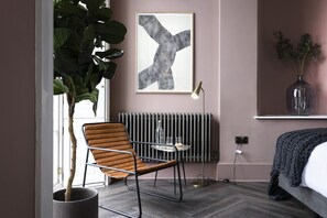 A modern bedroom with a bed, a radiator, a chair, a table, and a large plant. - City-Centre Studio in Historic Georgian Townhouse (Edinburgh)