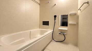 A bathroom with a bathtub, a handheld showerhead, and a built-in toilet.